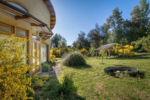 A house with a garden, a wooden deck, and a circular fire pit.