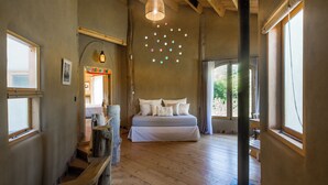 Een slaapkamer met een groot bed, houten vloeren, een hanglamp en uitzicht op de omgeving.