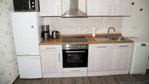 Una cucina compatta con mobili bianchi, una cappa aspirante in acciaio inox, un forno integrato, un microonde e una macchina da caffè.