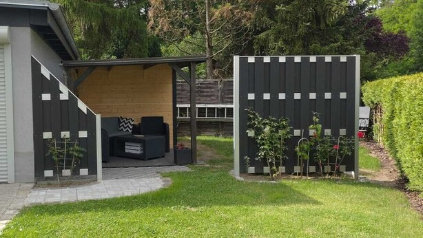 Un'area patio moderna all'aperto con una pergola in legno, una zona salotto e un giardino recintato.