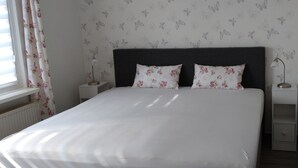 Un letto rifatto con cuscini floreali, un comodino con una lampada e una presa elettrica sulla parete.