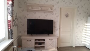 Una stanza con una televisione su un supporto in legno, una porta decorata con un cuore e una finestra con tende a motivi.