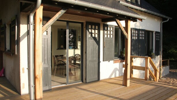 A wooden deck with a glass door leading to an interior dining area. - La Bellevue forest-edge cottage (Hénouville)