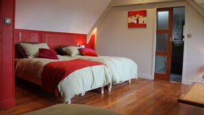 A bedroom with a sloped ceiling, a bed with multiple pillows, a red accent wall, and a wooden floor. - La Bellevue forest-edge cottage (Hénouville)