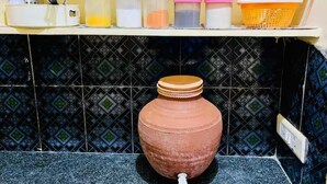 Une cuisine avec un grand pot en argile posé sur le comptoir, une étagère contenant divers récipients et un mur recouvert de carreaux.