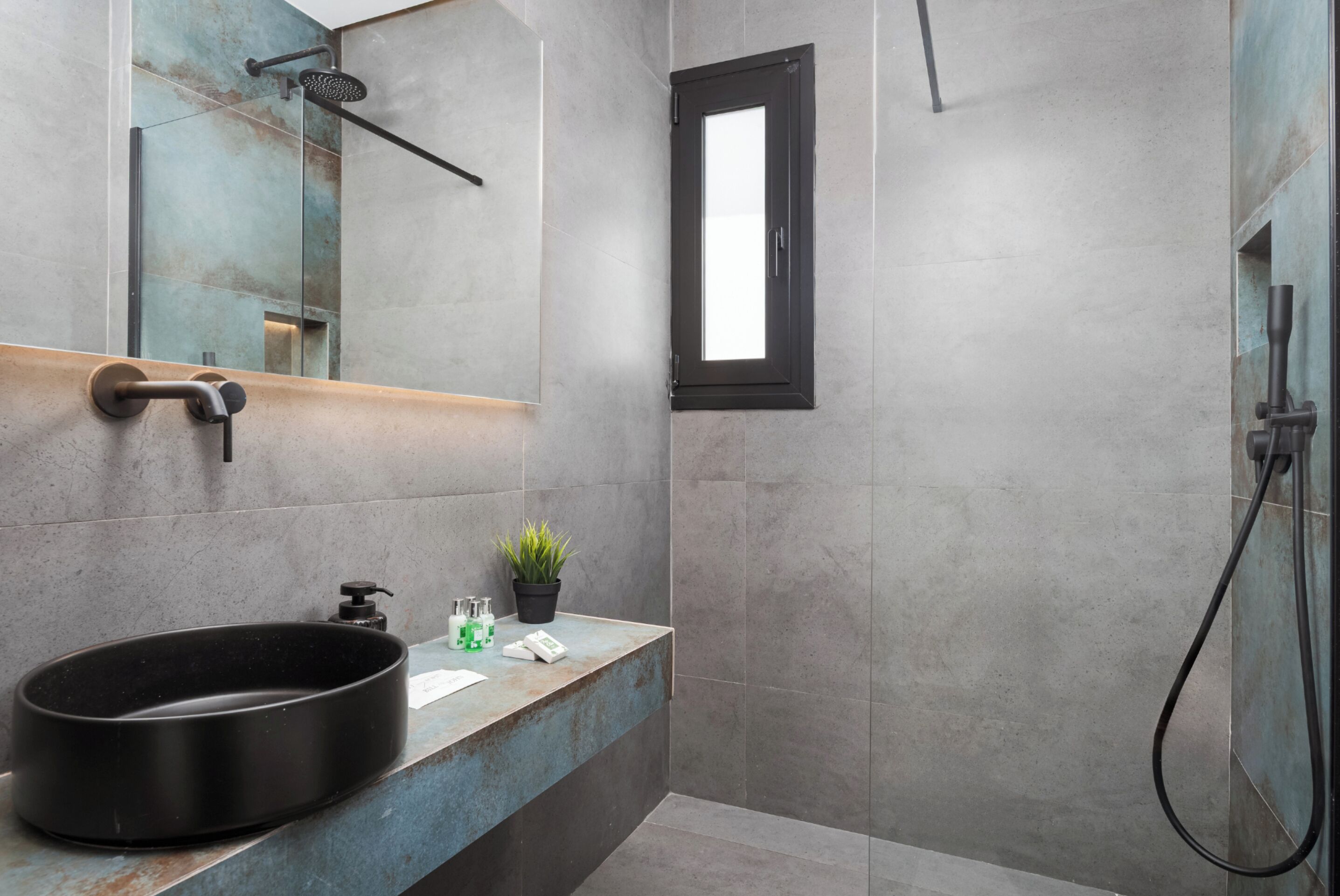 A modern bathroom with a large black basin, a mirror, a potted plant, and a shower.