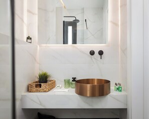 Ein Badezimmer mit Marmorwaschtisch, Spüle aus Kupfer, Spiegel und Dusche.