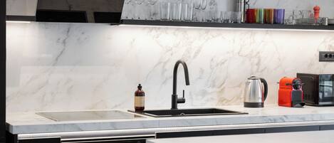 A modern kitchen with a marble countertop, stainless steel appliances, and a variety of glassware and kitchen tools.