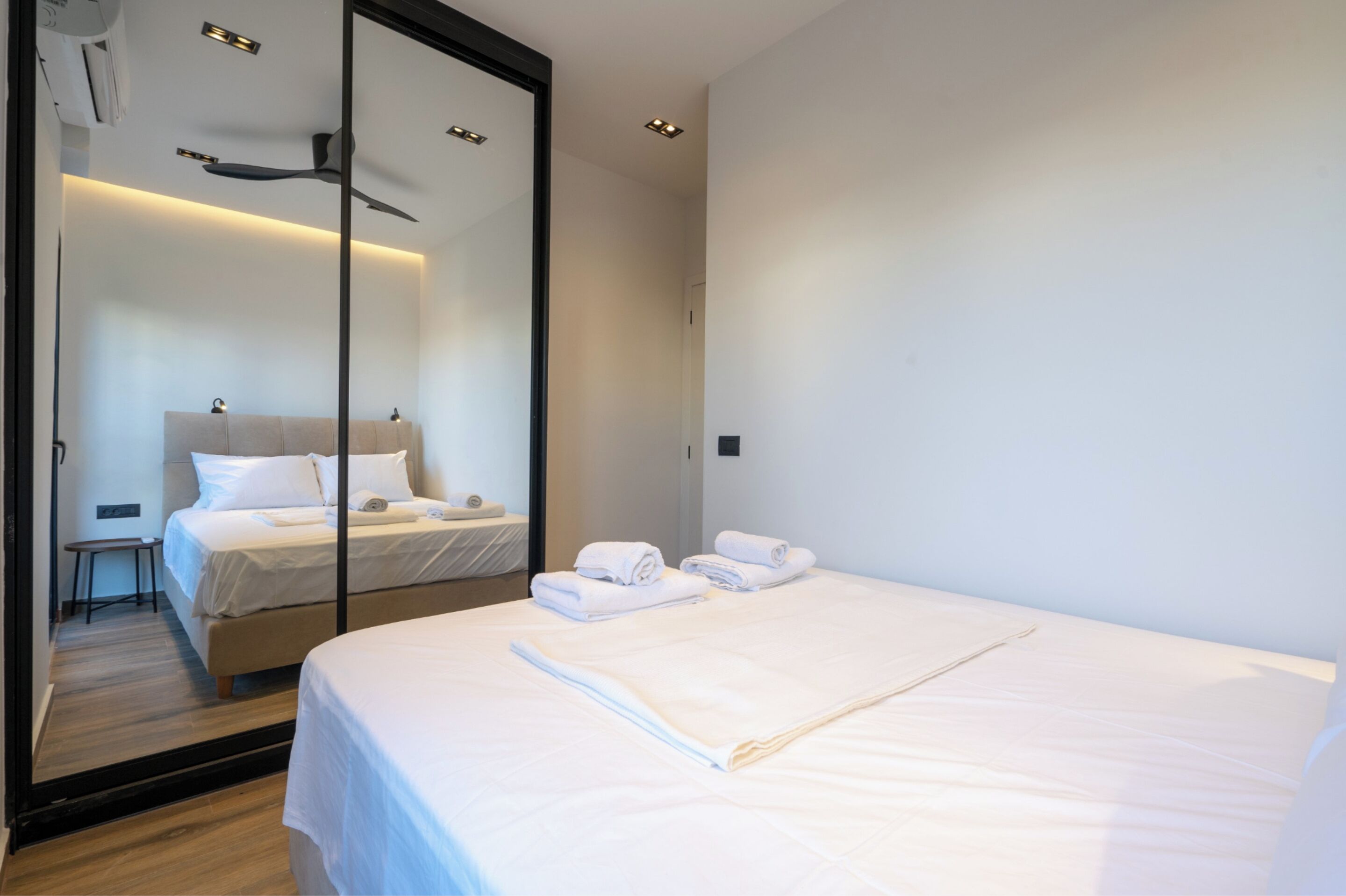 Moderni hotellihuone, jossa on suuri sänky, erillinen oleskelualue ja peili, joka heijastaa huonetta.