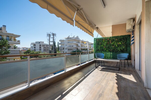 Ein Balkon mit Blick auf Gebäude, eine grüne Wand mit Pflanzen und zwei blaue Stühle.