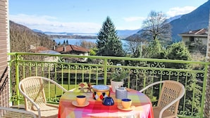 Un balcon avec une table dressée pour deux personnes, offrant une vue imprenable sur un lac pittoresque et les montagnes.