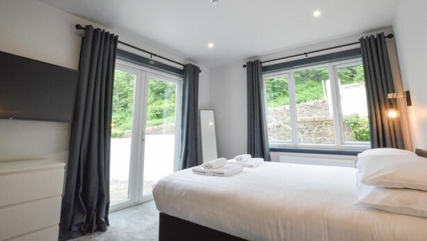 A hotel room with a bed, a flat-screen TV, and a large window with curtains. - The Righ (Oban)
