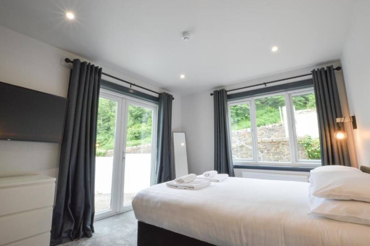 A hotel room with a bed, a flat-screen TV, and a large window with curtains.