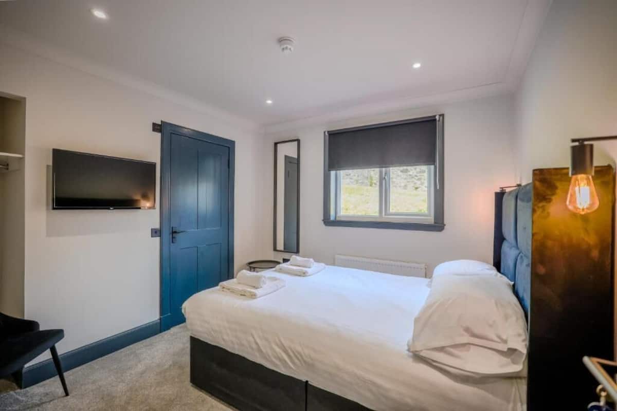A modern bedroom with a large bed, a TV mounted on the wall, a window with a view, and a door.