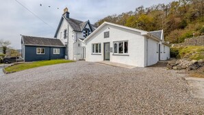 A two-story house with a gravel driveway and a stone wall. - The Righ (Oban)