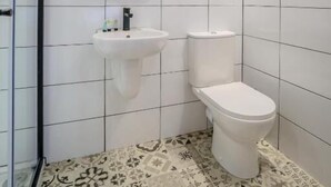 A bathroom with white tiled walls, a sink, and a toilet. - The Righ (Oban)