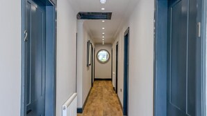 A narrow hallway with wooden flooring and blue doors on both sides. - The Righ (Oban)