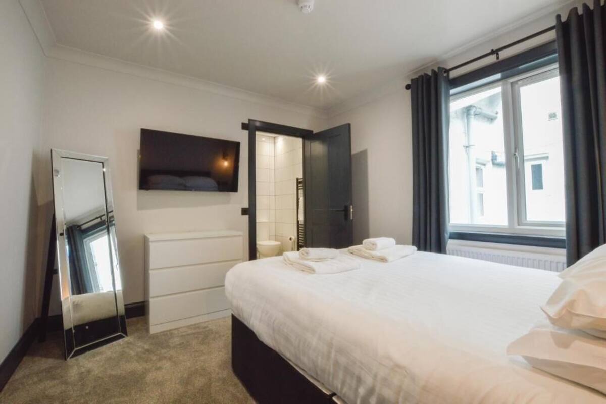 A hotel room with a bed, a flat-screen TV mounted on the wall, a wardrobe, and a window with curtains.