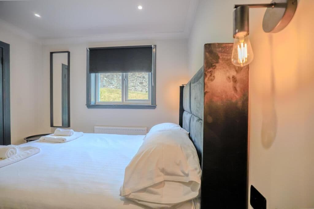 Una camera d'albergo con un letto, una finestra, uno specchio e una lampada fissata al muro.