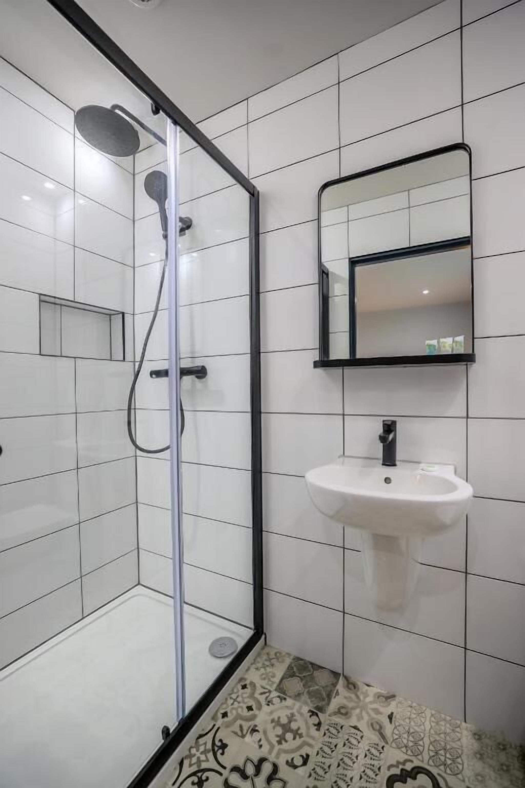Een moderne badkamer met een douchecabine van glas, een witte wastafel en een spiegel erboven.