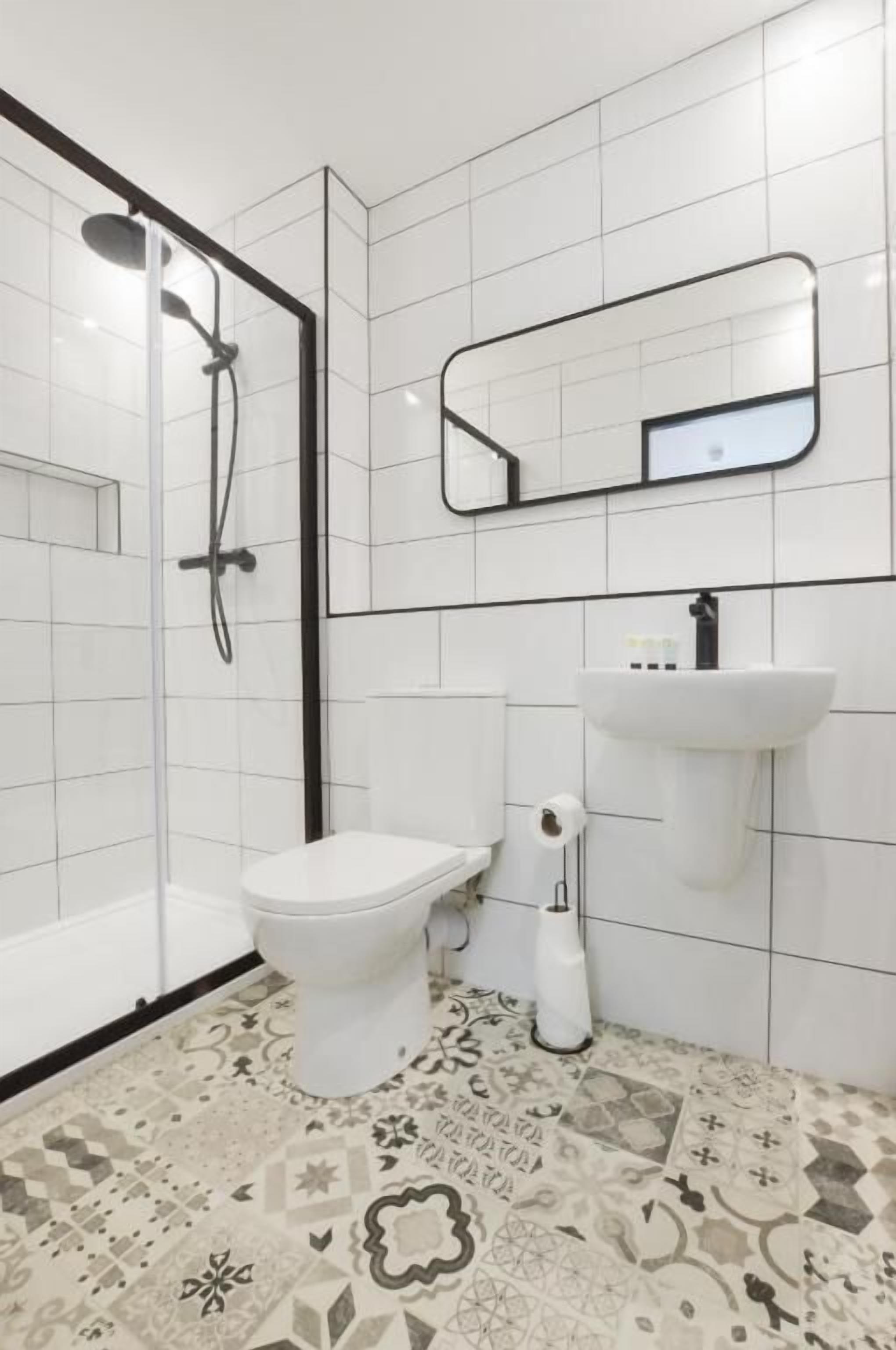 A modern bathroom with a glass-enclosed shower, a white toilet, a sink, and a patterned floor.