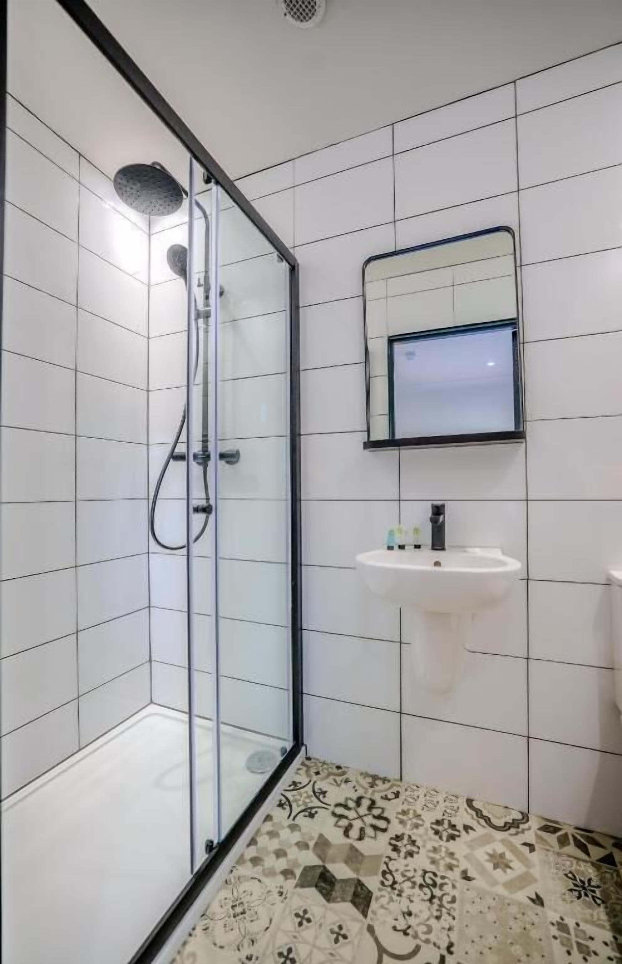 A modern bathroom with a glass shower enclosure, a white sink, and a mirror above it.