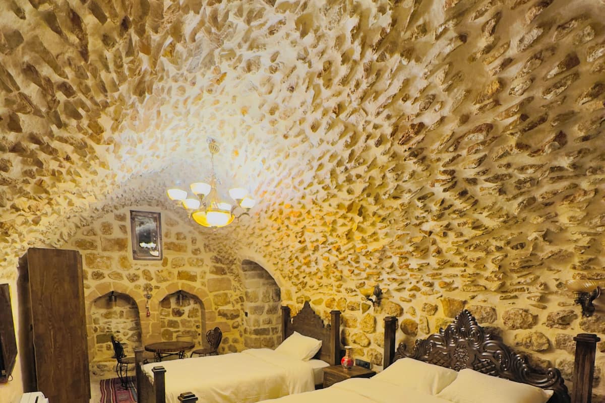 A stone-walled bedroom with two beds, a wooden headboard, and a small table.