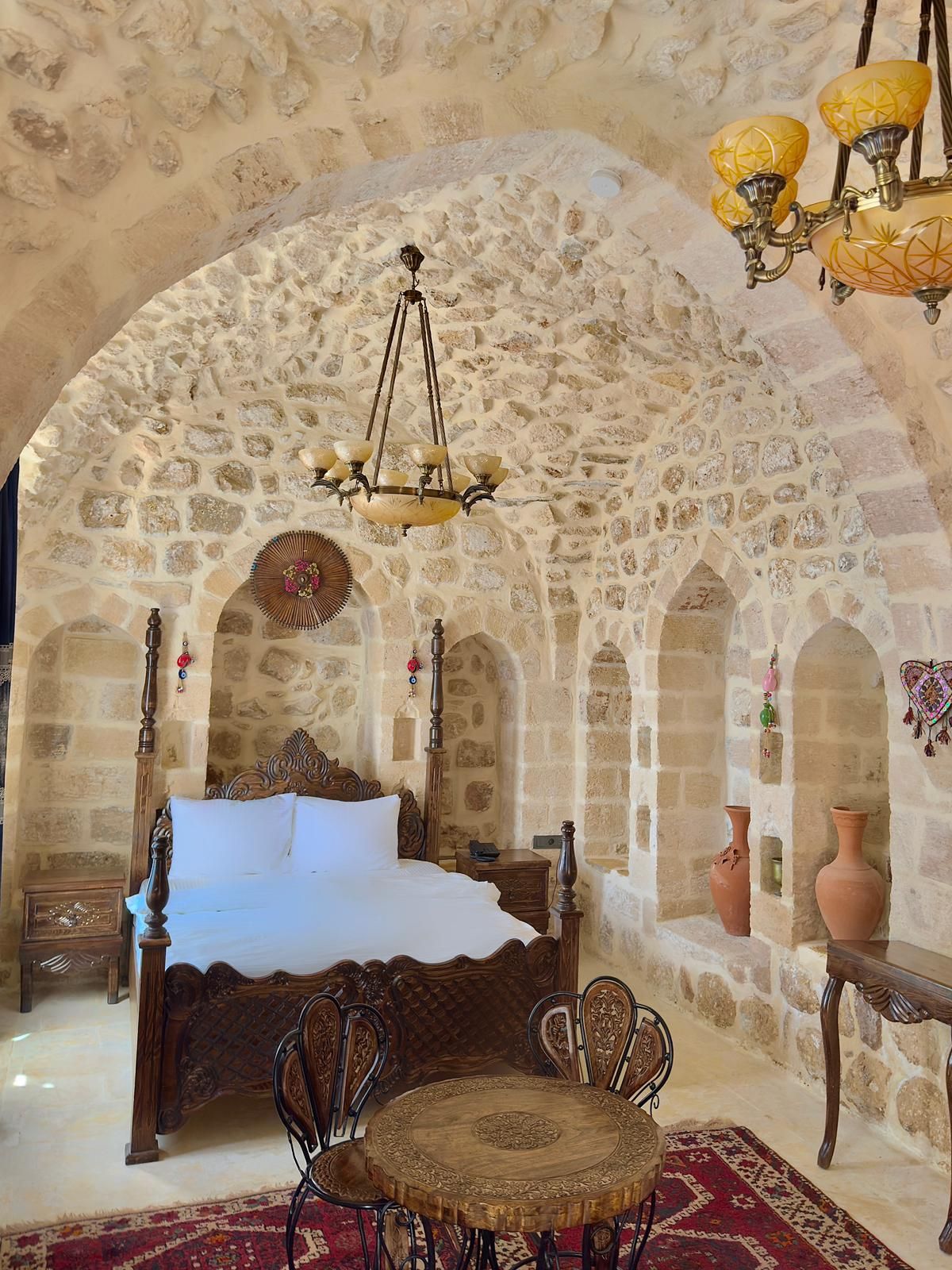 Un dormitorio con pared de piedra, una cama, un candelabro y una mesa con sillas.