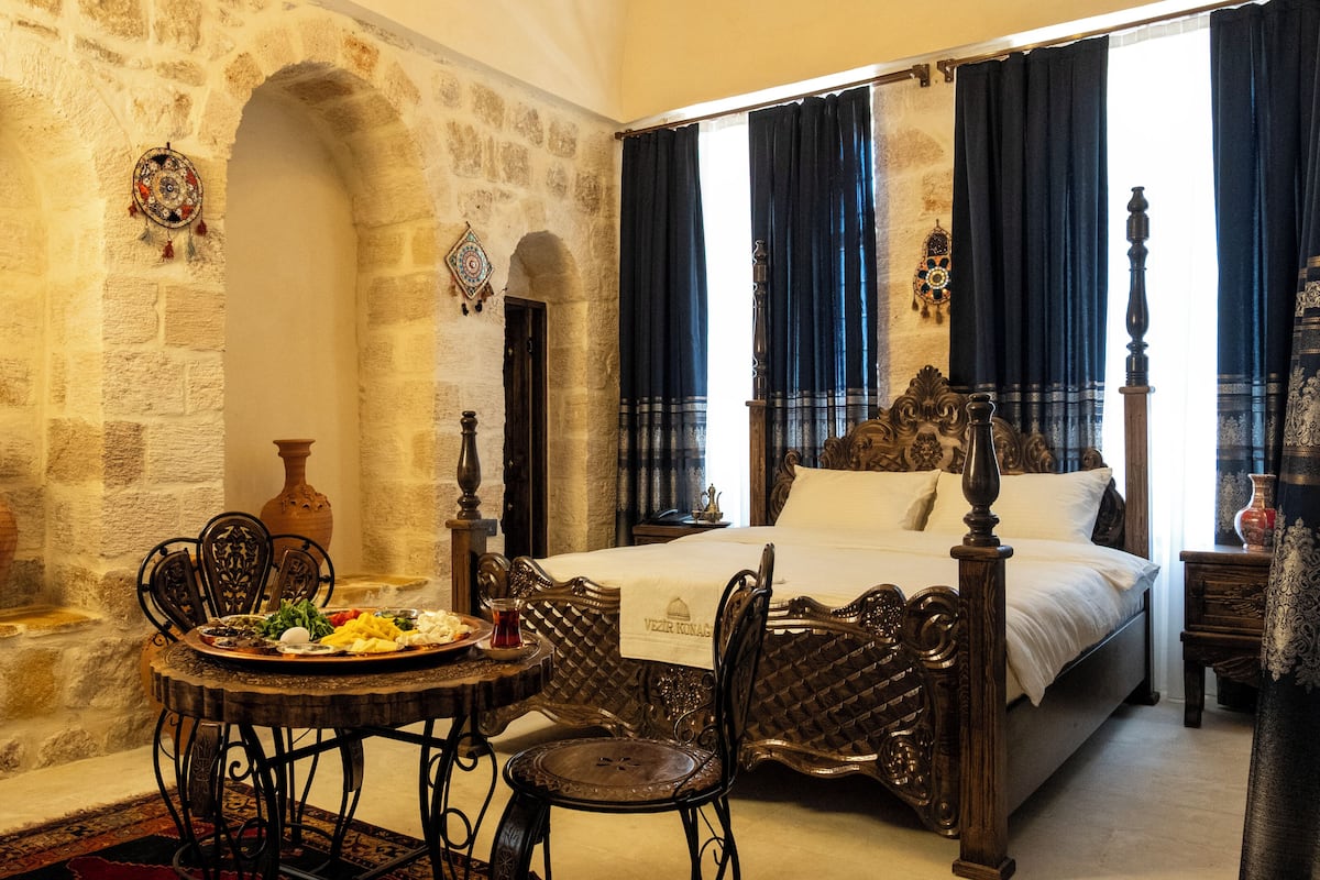 A traditional room with a stone wall, a bed with a canopy, and a dining table with chairs.
