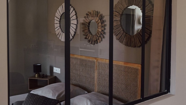 Ein Schlafzimmer mit einem Bett, einem Nachttisch, einer Lampe und zwei dekorativen Wandspiegeln.