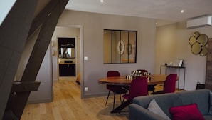 Ein modernes Wohnzimmer mit Essbereich, mit einem Holztisch, roten Stühlen und einem grauen Sofa mit rotem Kissen.