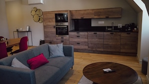 Ein modernes Wohnzimmer mit grauem Sofa, einem Holztisch und einer Küche mit Holzschränken und Geräten.