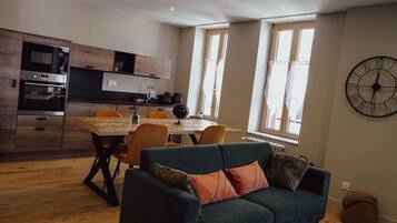 A modern kitchen with a dining area, a large clock on the wall, and a cozy seating area with a sofa and chairs.