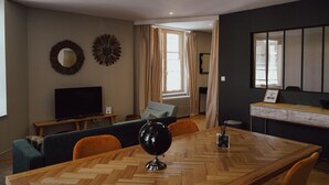 A modern living room with a wooden dining table, a television, and a sofa. - Les Résidences Gueguen - Suite Les Clos (Chablis)