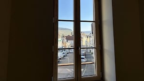 A room with a large window overlooking a street with parked cars and buildings. - Les Résidences Gueguen - Suite Les Clos (Chablis)
