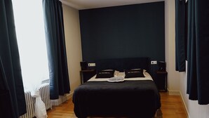 A bedroom with a black bedspread, two bedside tables with lamps, and a radiator.