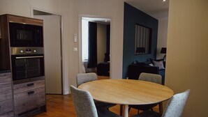 A dining area with a round table and four grey chairs, a built-in oven, and a blue accent wall.