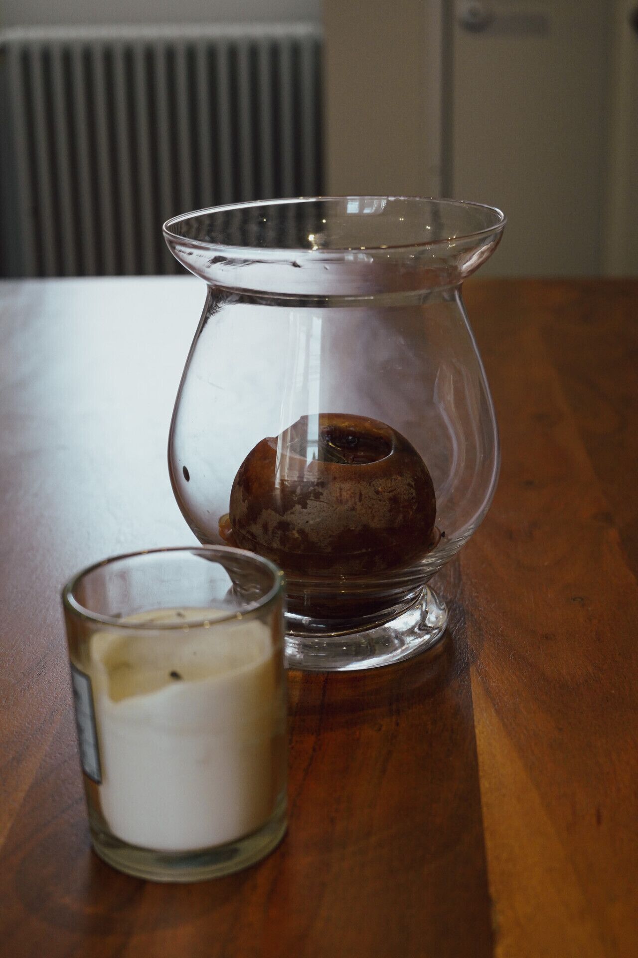 Un candelabro de vidrio transparente con una vela en su interior, sobre una mesa de madera.