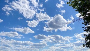 Un paysage rural avec une ville qui se dessine à l’horizon, des champs verdoyants et un ciel dégagé parsemé de nuages.