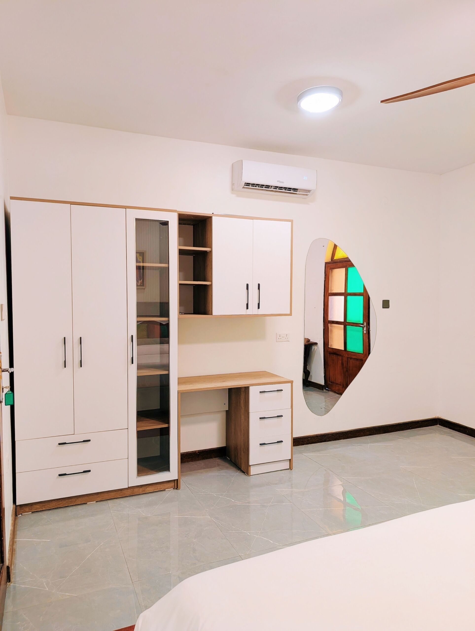 A room with a wardrobe, a desk, a mirror, and an air conditioning unit.