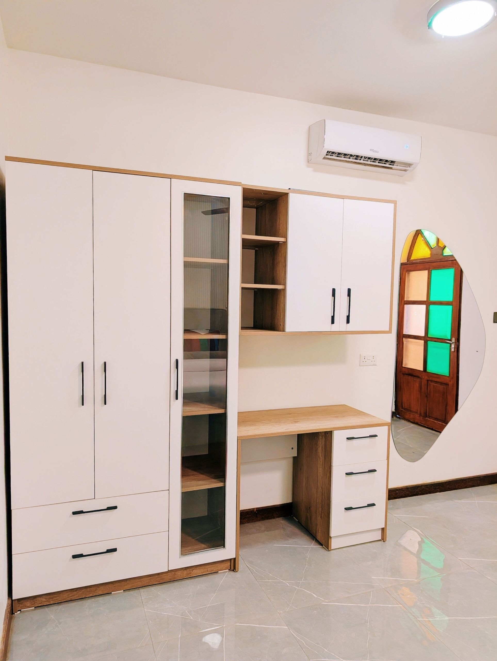 Una habitación con un armario blanco, un escritorio de madera y un espejo.