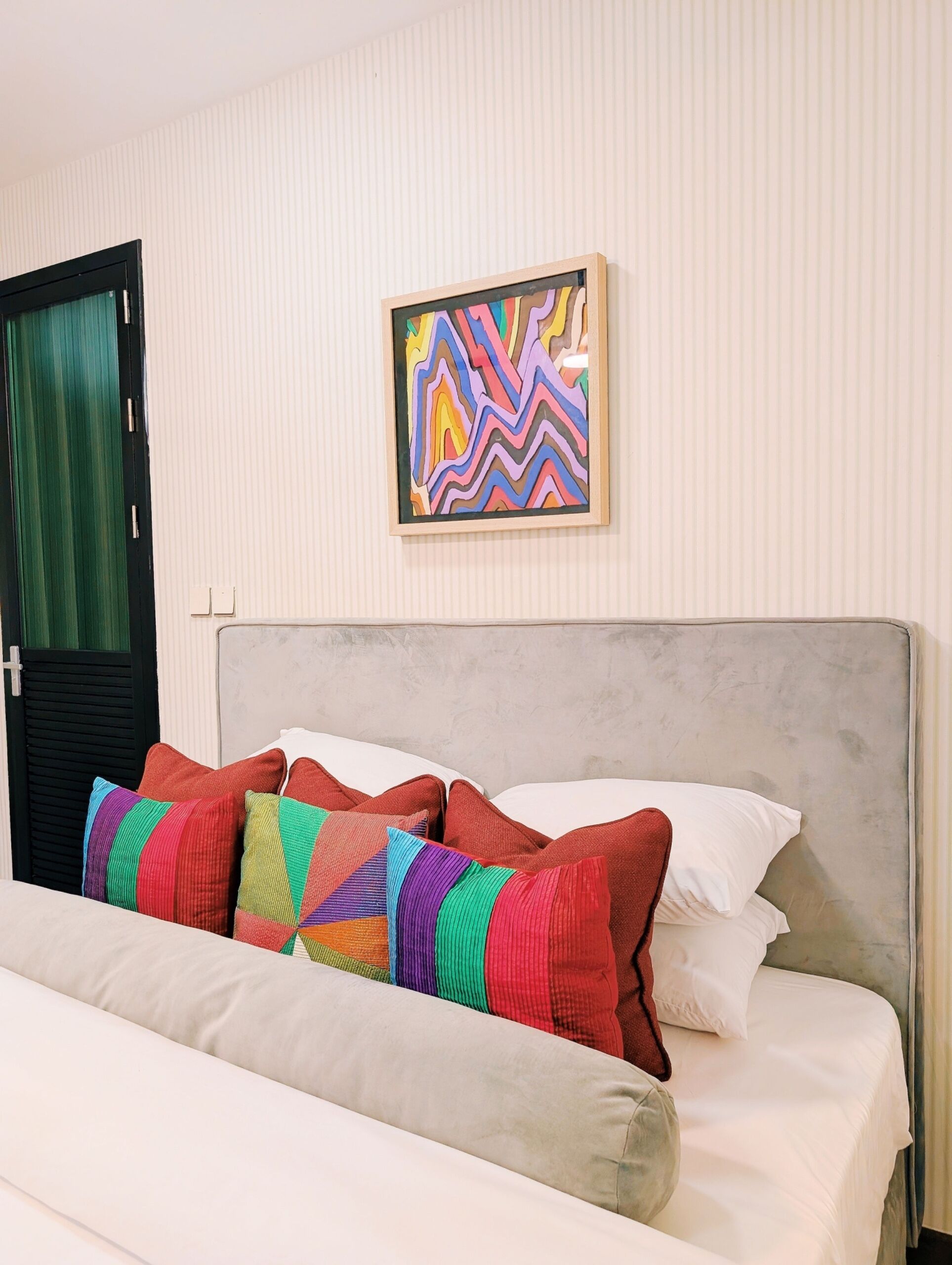 A bed with colorful pillows, a gray headboard, and a striped wall.