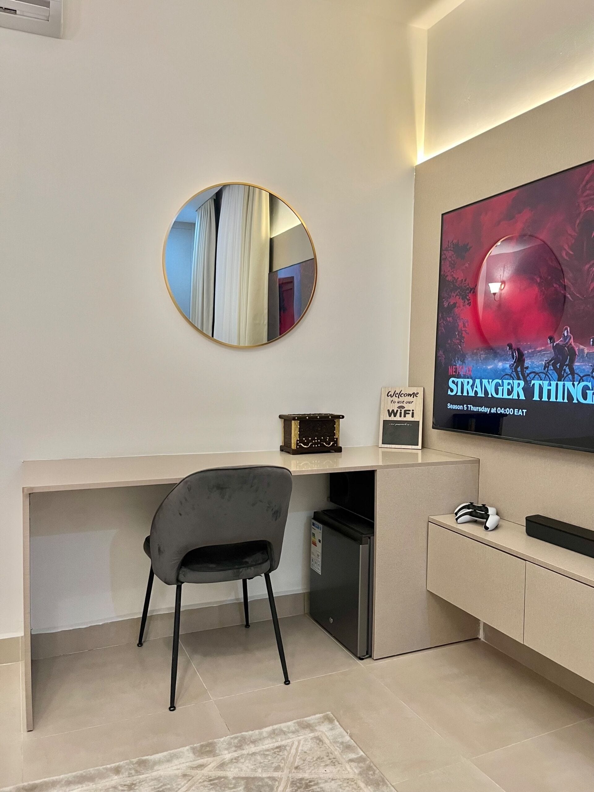 A modern living room with a flat-screen TV, a round mirror, a small table, a chair, and a rug.