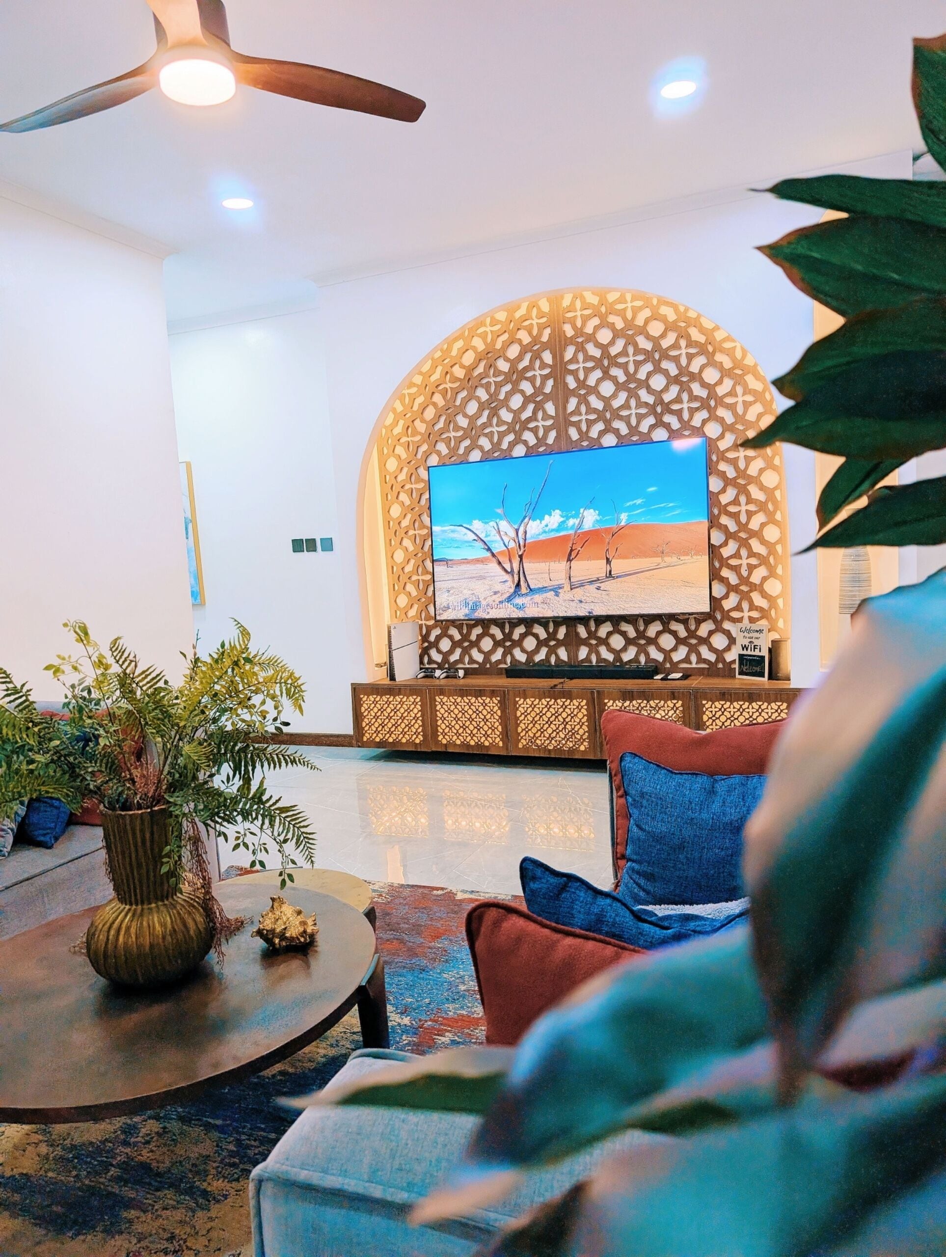 Una sala de estar moderna con un televisor de pantalla plana montado en una pared decorativa, un ventilador de techo y una mesa de centro con una planta.