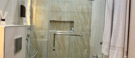 A modern bathroom with a glass shower enclosure, a toilet, and a towel rack.