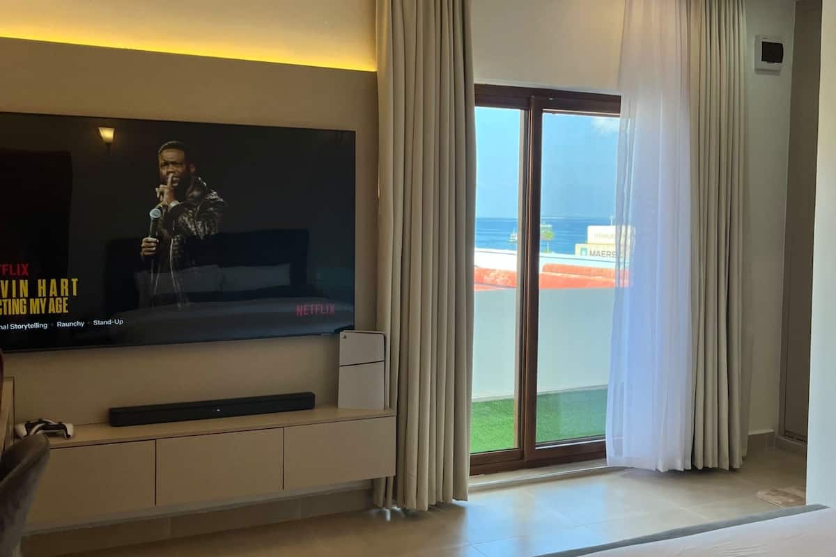 Hotellihuone, jossa on suuri litteänäyttöinen televisio, sänky, työpöytä ja ikkunasta avautuva näkymä merelle.