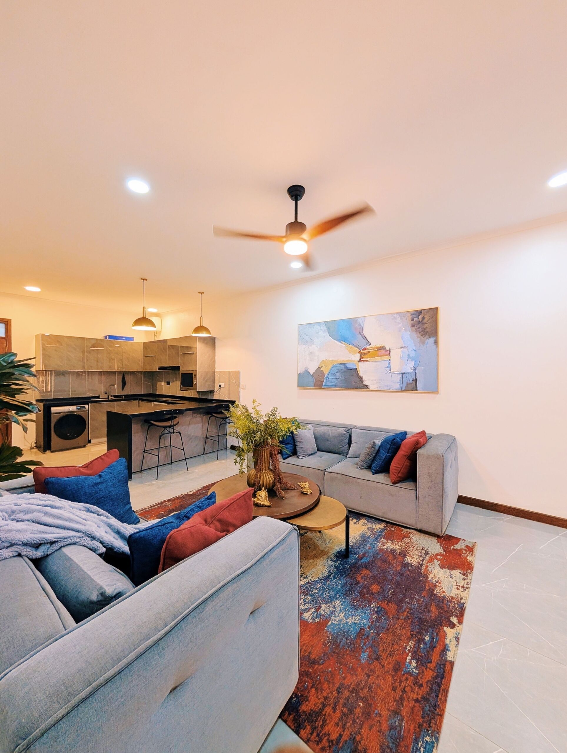 A modern living room with a grey sofa, a coffee table, and a kitchen area in the background.