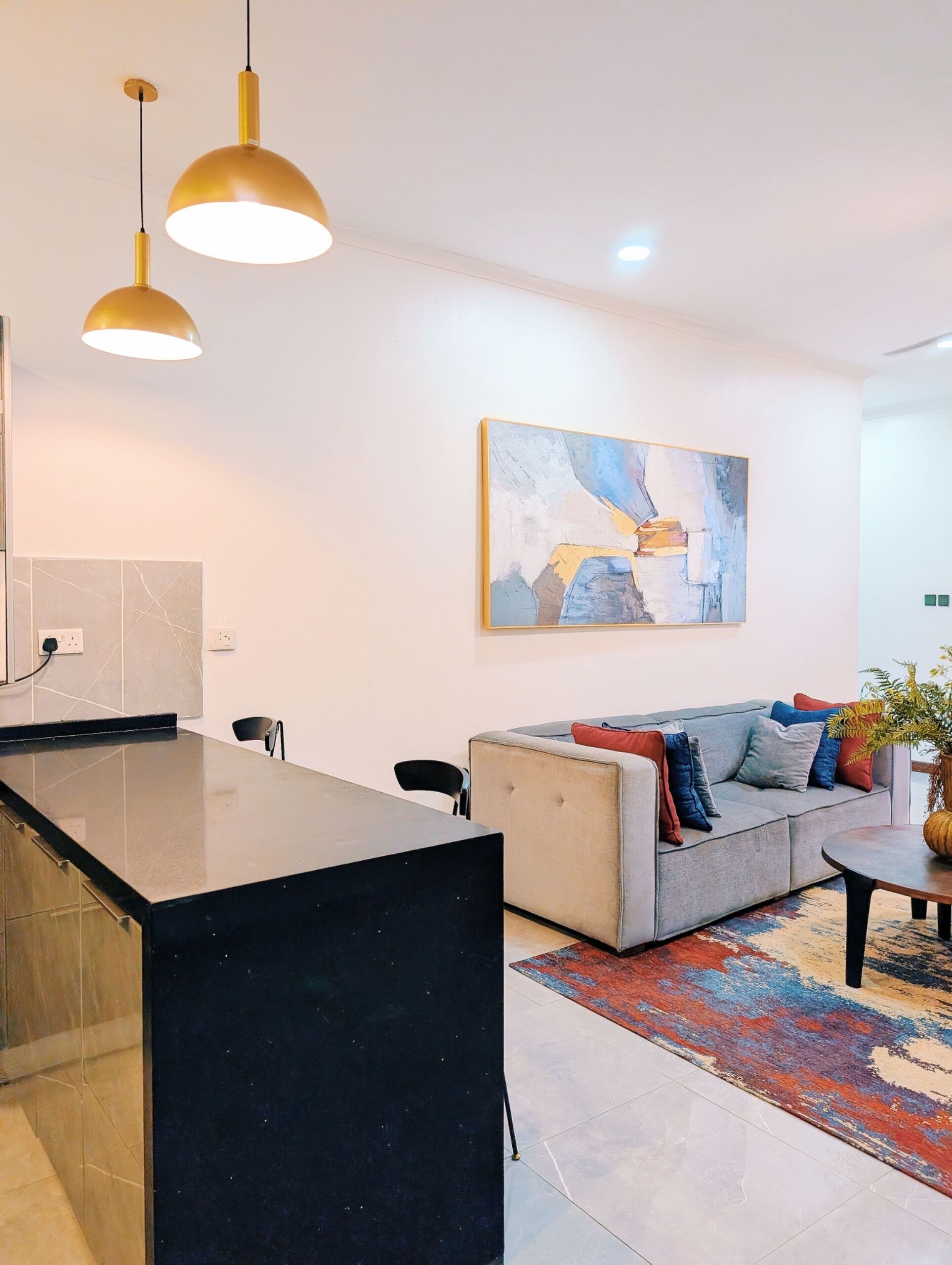 A modern kitchen with a black countertop, a grey sofa with colorful cushions, and a large abstract painting on the wall.