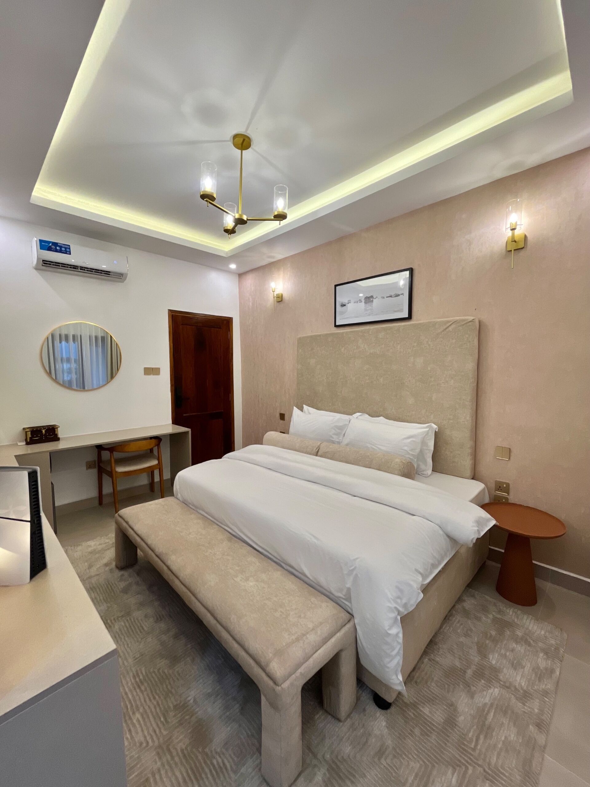 A modern hotel room with a large bed, a desk, a chair, and a small table.