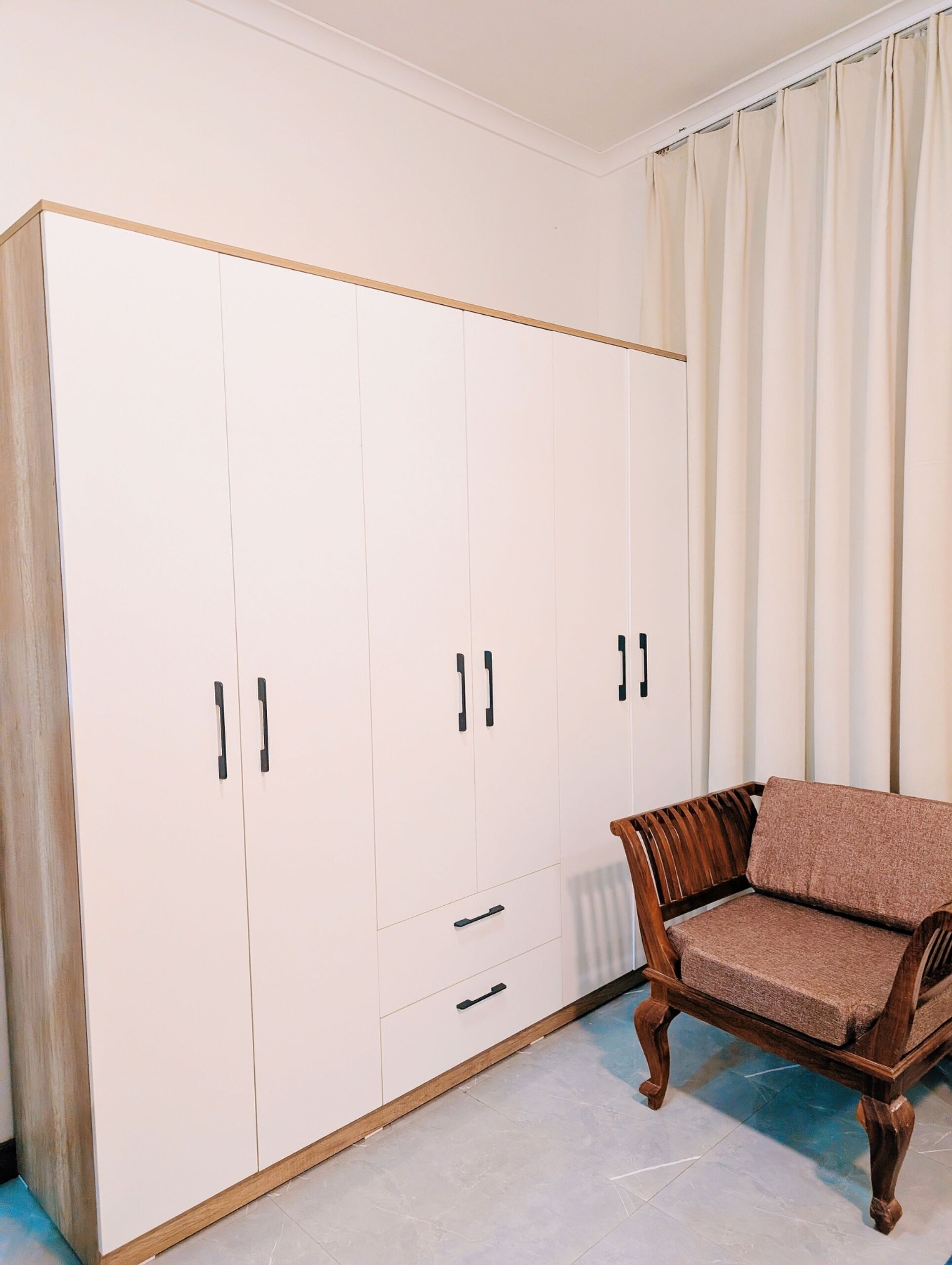 Une pièce avec une grande armoire, une chaise en bois et une fenêtre avec des rideaux.